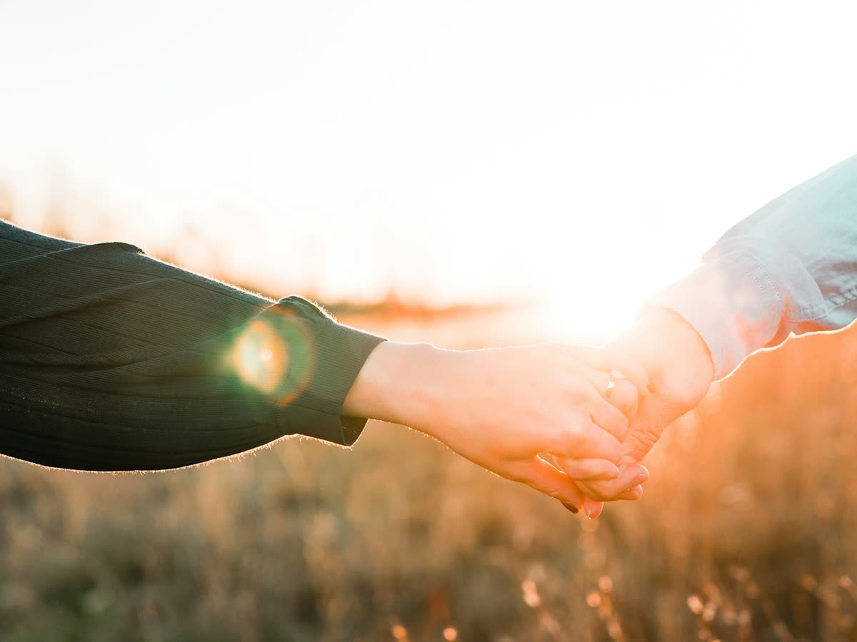 Two hands reaching for each other in golden evening light, a symbol of support